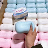 A hand is holding a light blue squishy soap shape fidget toy surrounded by many white and pink soap shapes.