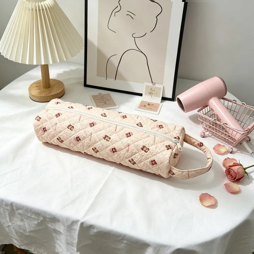 A quilted pink cotton hair dryer storage bag with a handle resting on a white tablecloth next to a pink hair dryer and a wick
