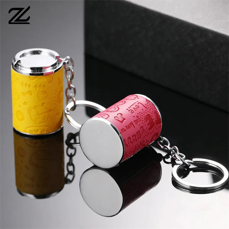 A silver metal coin tube keychain with a yellow and pink design, shown against a dark background.
