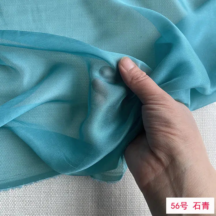 A hand is gently folding a piece of light blue sheer chiffon fabric.