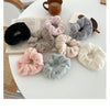 A collection of plush coil hair ties in various shades of gray, pink, and black are displayed on a white surface next to a cu