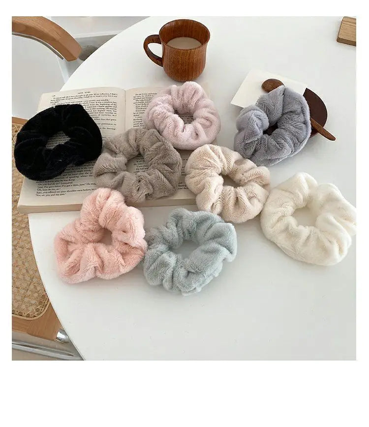 A collection of plush coil hair ties in various shades of gray, pink, and black are displayed on a white surface next to a cu