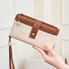 A hand holds a beige leather bifold wallet with a brown closure and strap, demonstrating RFID protection.
