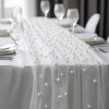 A white pearl beaded tulle table runner draped over a white tablecloth for an elegant wedding or event setting.