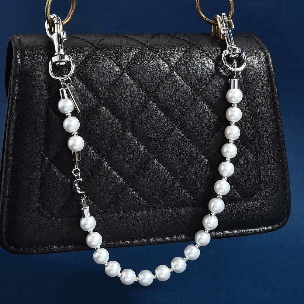 A silver chain necklace with pearl beads and a letter C charm hanging over a black quilted purse.