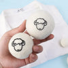 A hand holds two white wool dryer balls, each featuring a black outline of a face.
