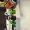 A close-up view of a magnetic wall-mounted spray can organizer with silver and black cans and green plastic holders.