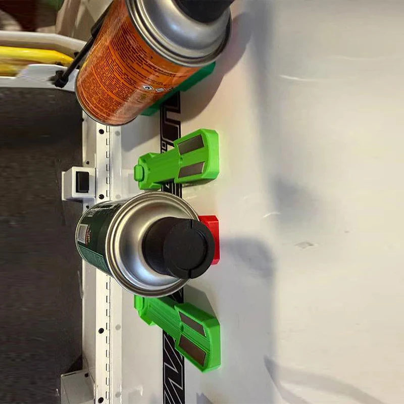 A close-up view of a magnetic wall-mounted spray can organizer with silver and black cans and green plastic holders.