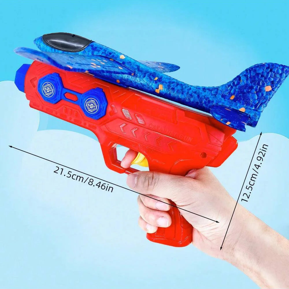 A hand holds a red foam catapult glider plane toy with blue and yellow accents against a light blue background.