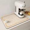 A white espresso machine is placed on a beige counter mat with gold trim, next to a white cup of coffee.