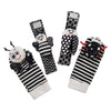 A set of soft baby wrist rattles and foot finder socks featuring black and white patterns with cute animal designs.