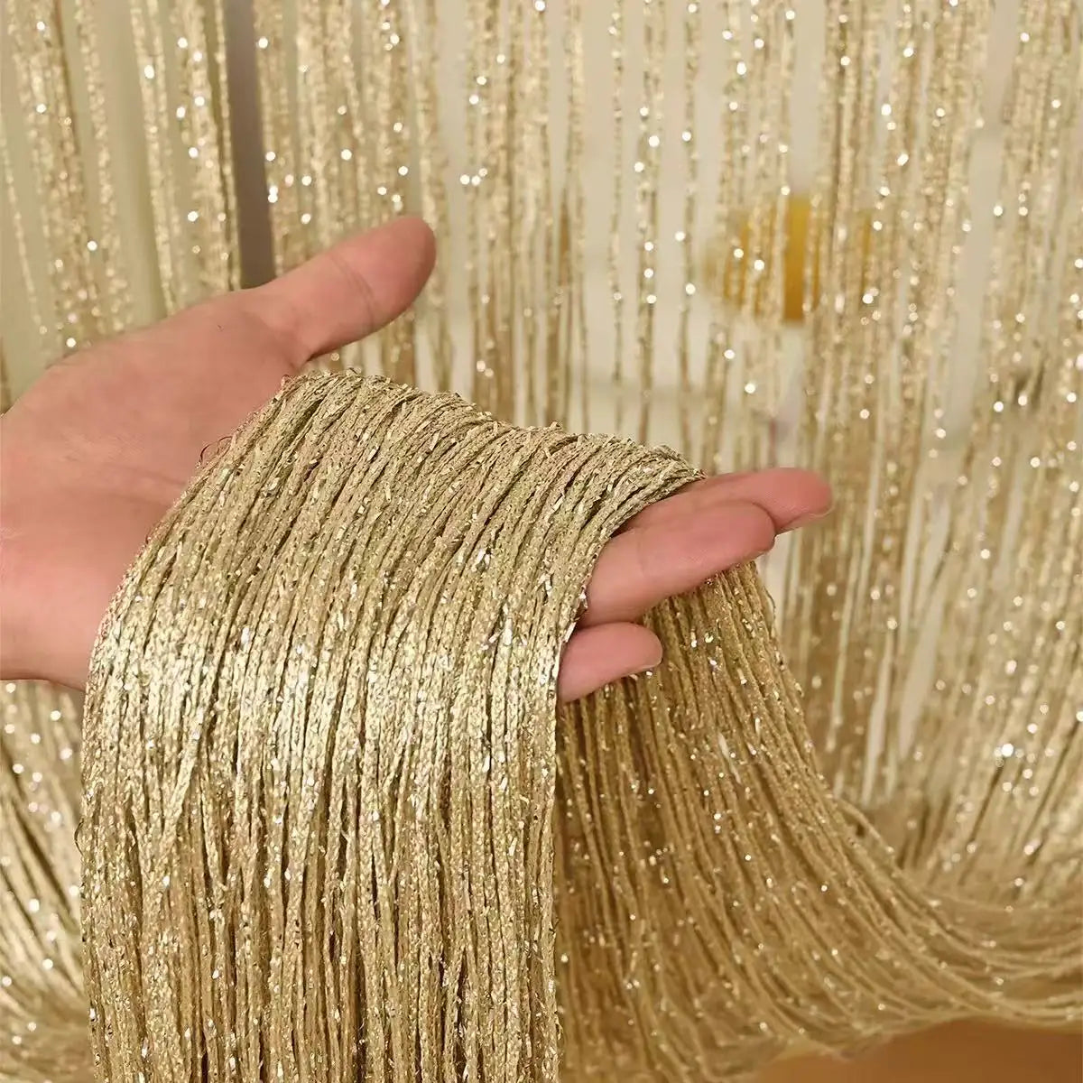 Eine Hand hält einen dicken, goldenen, perlenbesetzten Drahtvorhang zur Dekoration.