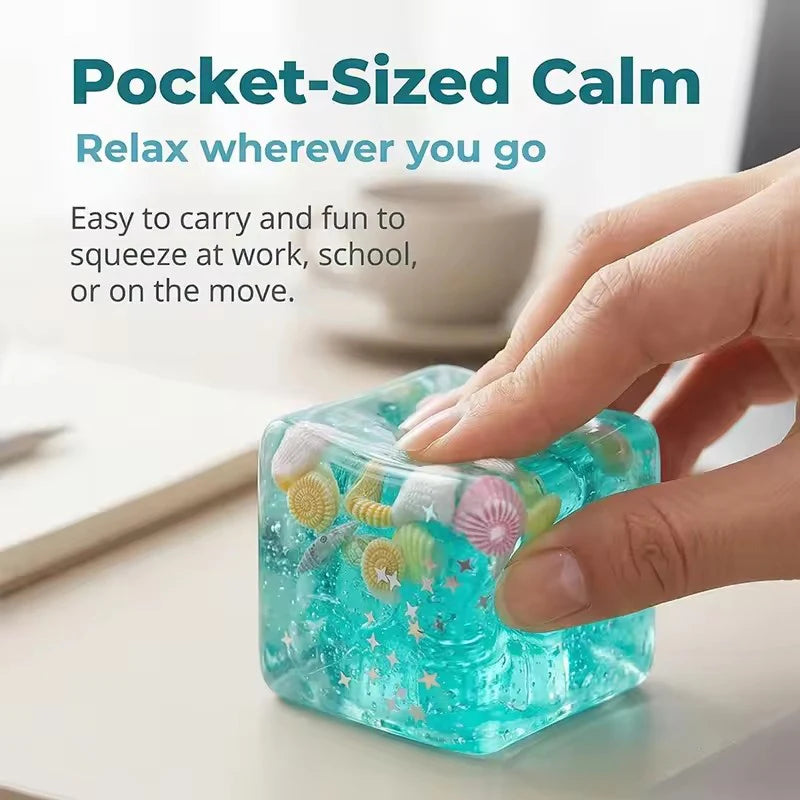 A hand is squeezing a translucent blue squishy ocean shell cube stress relief fidget toy on a white surface.