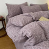 A set of soft printed duvet covers and pillowcases in a muted mauve color are displayed on a bed.
