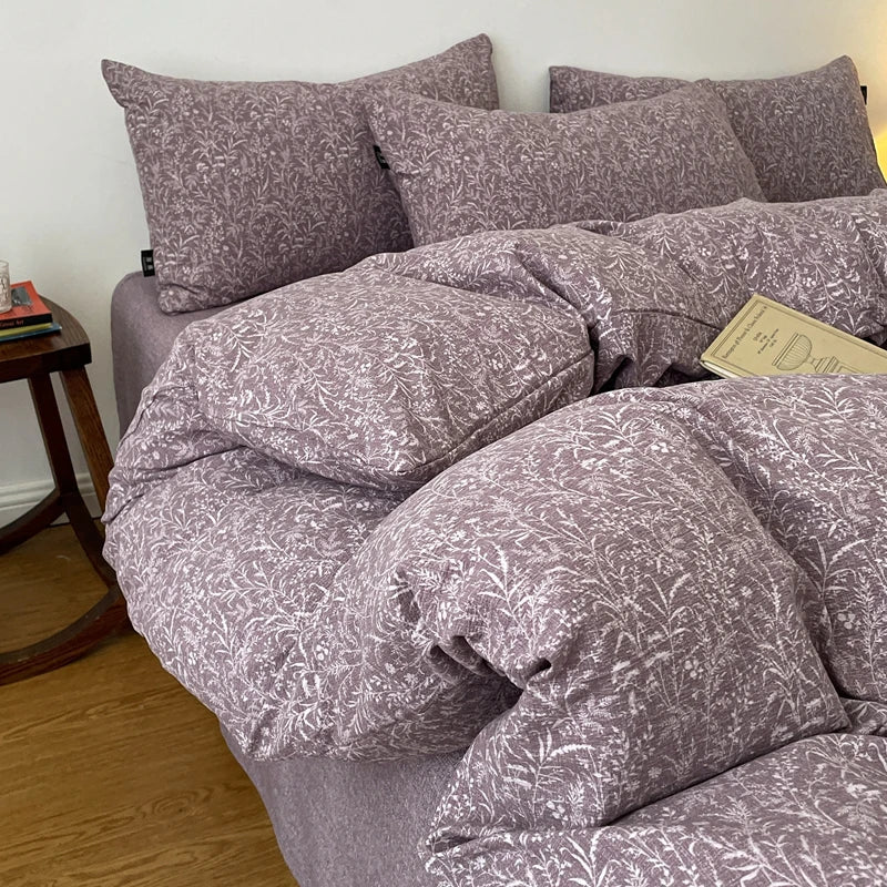 A set of soft printed duvet covers and pillowcases in a muted mauve color are displayed on a bed.