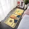 A yellow banknote pattern anti-slip soft floor mat lying on a dark floor next to a bed.