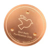 A round, copper purification disk for a bird bath, featuring a silhouette of a bird and text indicating 99.9% pure copper.