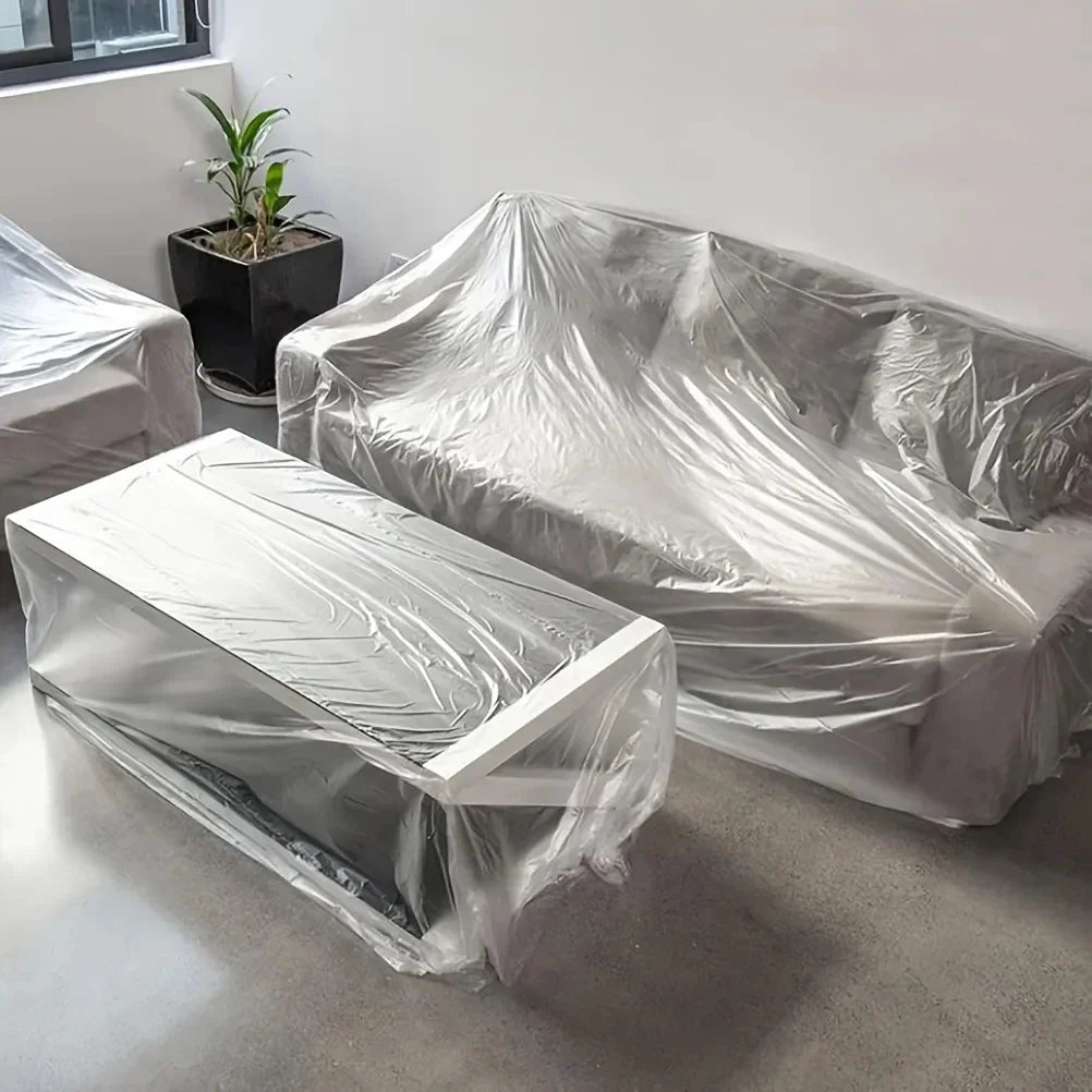 A clear plastic sheeting covers a sofa and a cabinet on a floor, used for painting and protection.