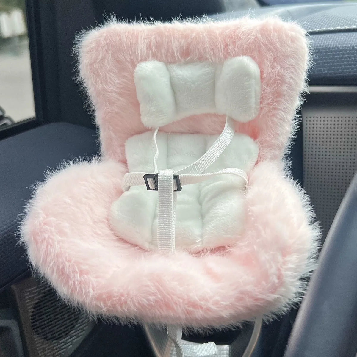 A pink and white faux fur miniature doll seat car vent decoration is shown inside a car interior.