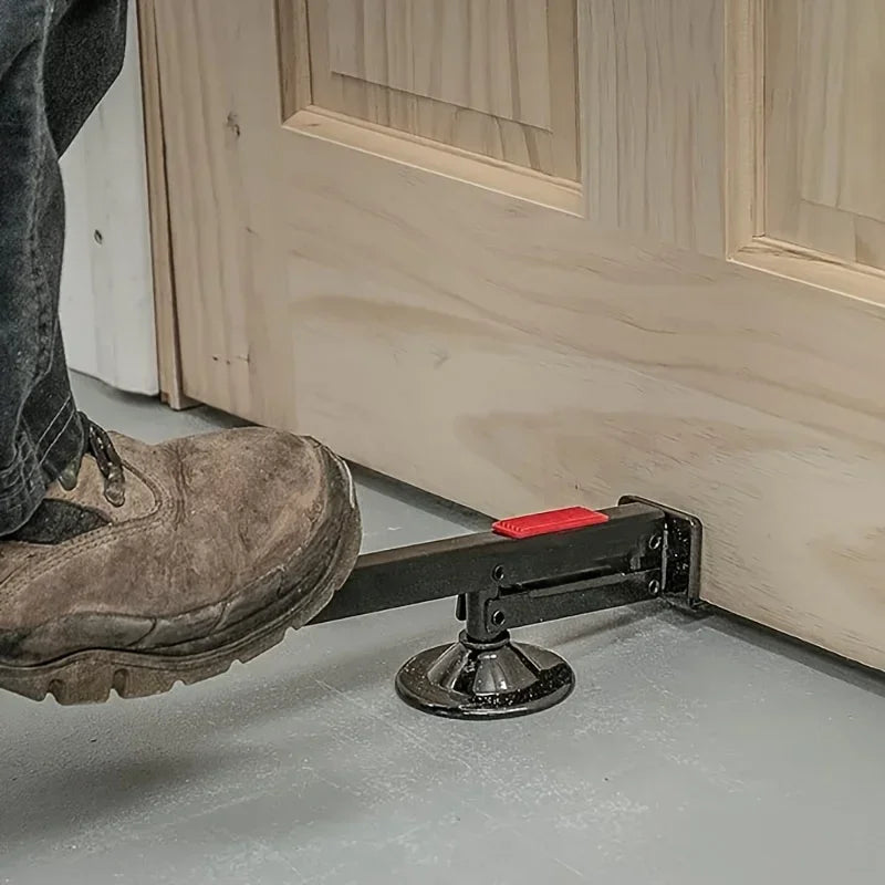A heavy-duty steel door lift tool is shown resting on a light gray floor next to a wooden door frame.