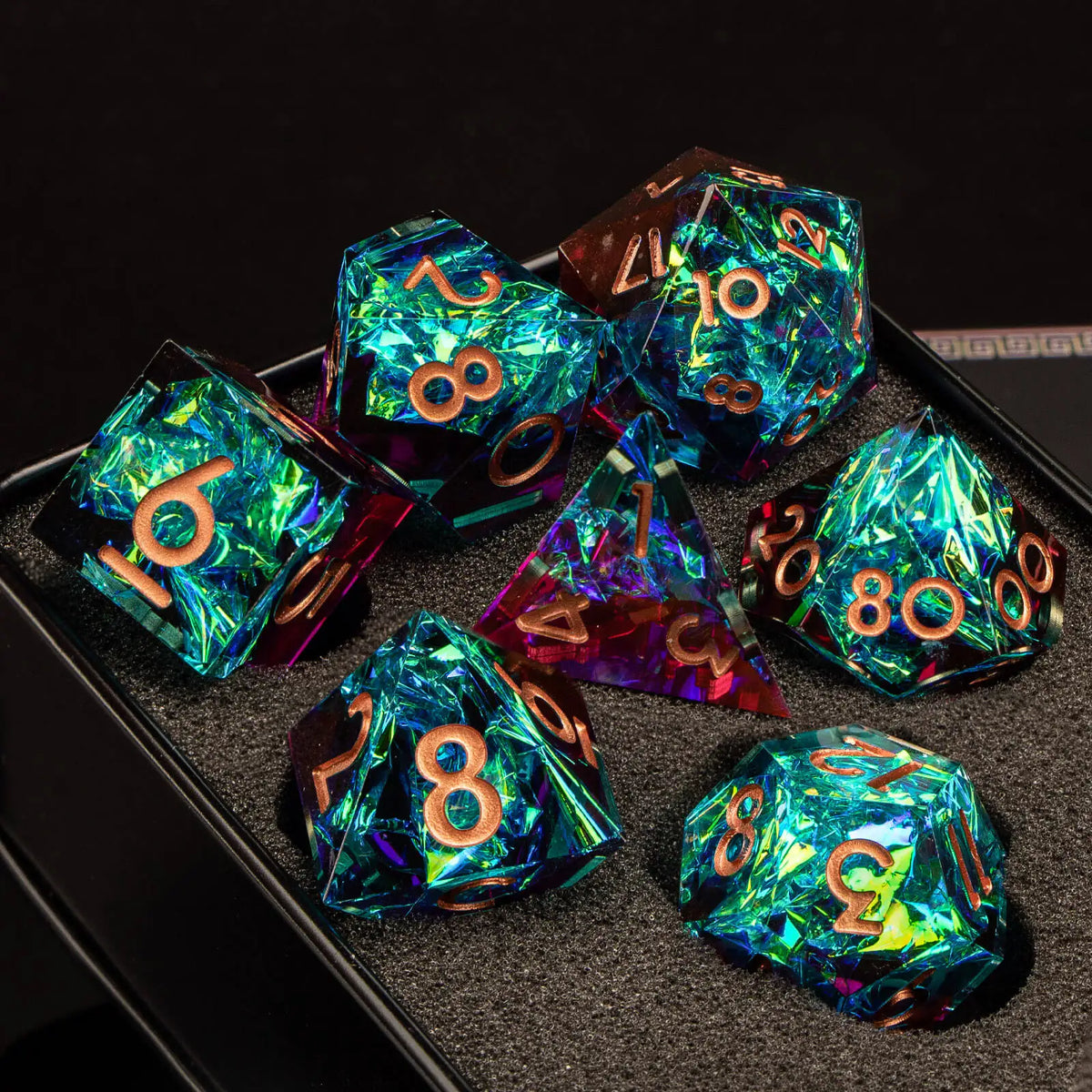 A collection of handmade resin polyhedral dice in various colors and angles resting on a dark surface.
