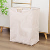 A beige striped foldable laundry basket with handles is shown on a wooden floor.