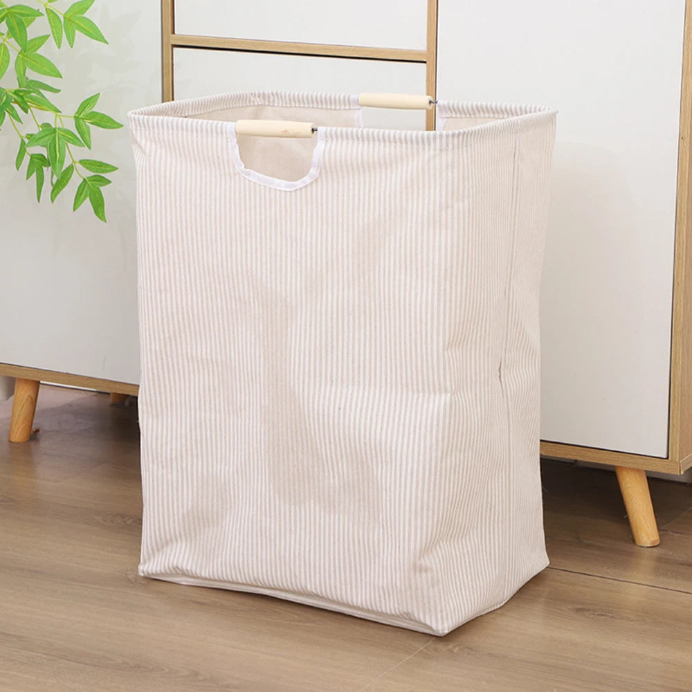 A beige striped foldable laundry basket with handles is shown on a wooden floor.