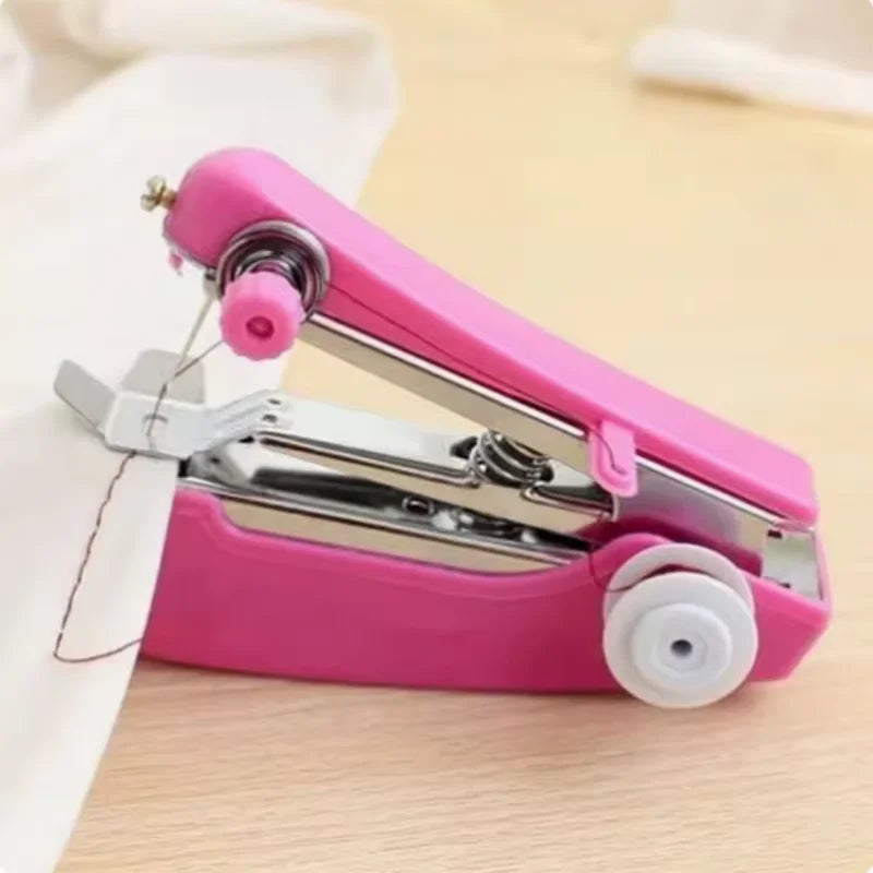 A pink portable handheld sewing machine is shown on a wooden surface.
