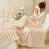 A fluffy cream flannel blanket draped over a white sofa, with a person adjusting it in a bright room.