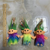 Three handcrafted troll doll figurines with bright green and purple hair standing on a gray surface.