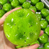 A hand holds a bright green, translucent squishy stress relief fidget ball surrounded by other similar balls.