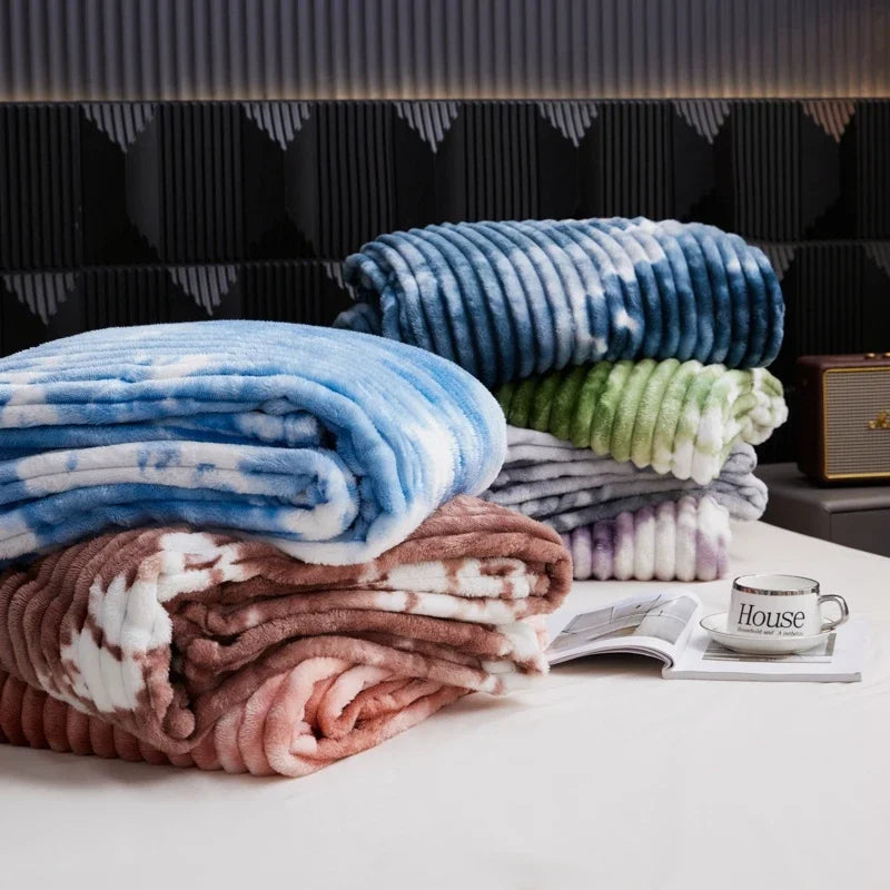 A stack of cozy flannel fleece throw blankets in shades of blue, green, and brown are displayed on a white surface.