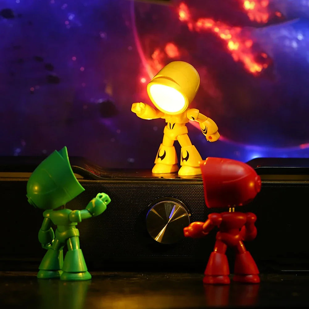 A bendable robot night light with a soft yellow glow is displayed on a dark surface against a colorful, cosmic background.