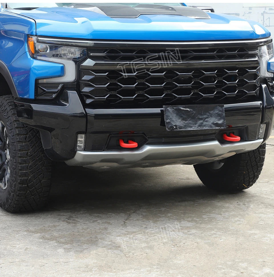 Close-up of a blue Chevrolet Silverado front grille and bumper with an aftermarket black tow hook cover.