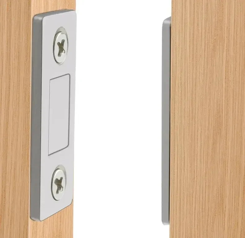 A close-up view of a silver magnetic door catch with two visible screws mounted on a light wood cabinet door frame.