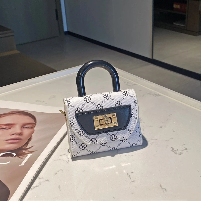 A small white and black patterned leather crossbody tote bag with a black handle resting on a white marble surface.
