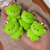 Five small, soft green alien plush toys with yellow antennae are held in a person's hand.