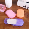 Three colored portable disposable soap tablets in pink, orange, and purple are displayed on a wooden surface.