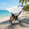A beige and white stretchable UV-protective stroller sun shade is placed on a wooden deck near the ocean.