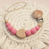 A wooden pacifier clip with crochet beads and a chain rests on a white, textured surface.