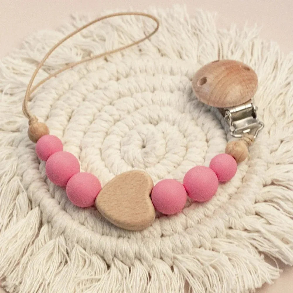A wooden pacifier clip with crochet beads and a chain rests on a white, textured surface.