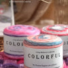 A spool of colorful Gradient cake yarn is displayed on a purple knitted fabric.