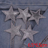 A set of five silver glitter star iron-on embroidered patches placed on a denim fabric.