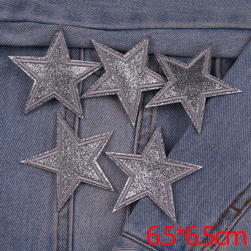 A set of five silver glitter star iron-on embroidered patches placed on a denim fabric.