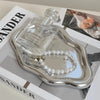 A clear glass bottle of Dolce & Gabbana perfume rests on a silver cloud-shaped jewelry tray with a pearl necklace.