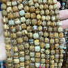 A hand holds a strand of natural stone square faceted beads for jewelry making.