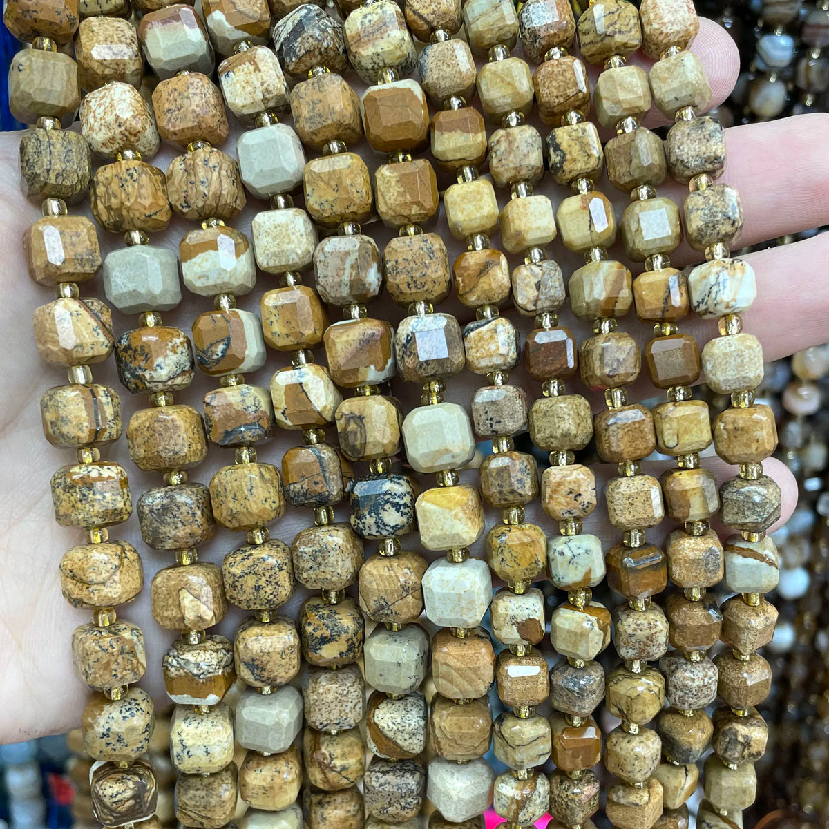 A hand holds a strand of natural stone square faceted beads for jewelry making.