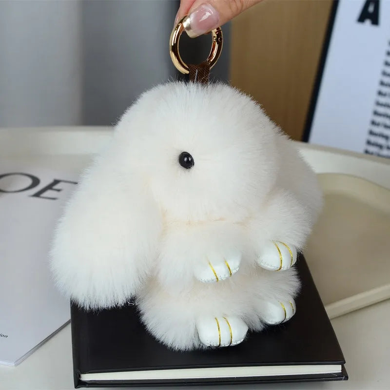 A white fluffy angel bunny keychain with a pom pom tail is displayed on a black book.