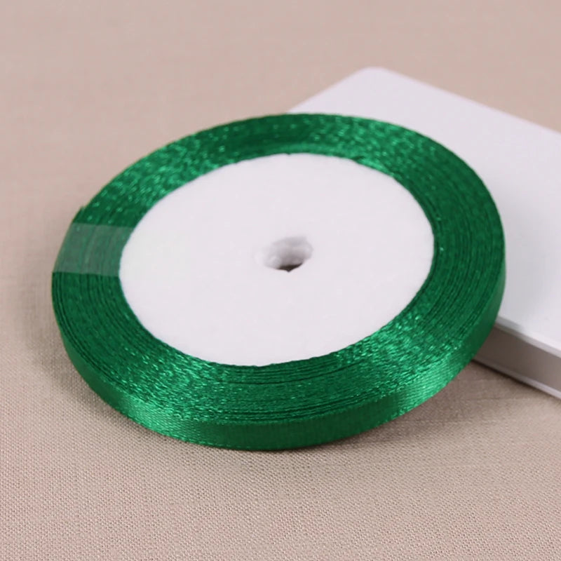 A roll of lustrous satin ribbon in emerald green with a white core, resting on a light beige surface.
