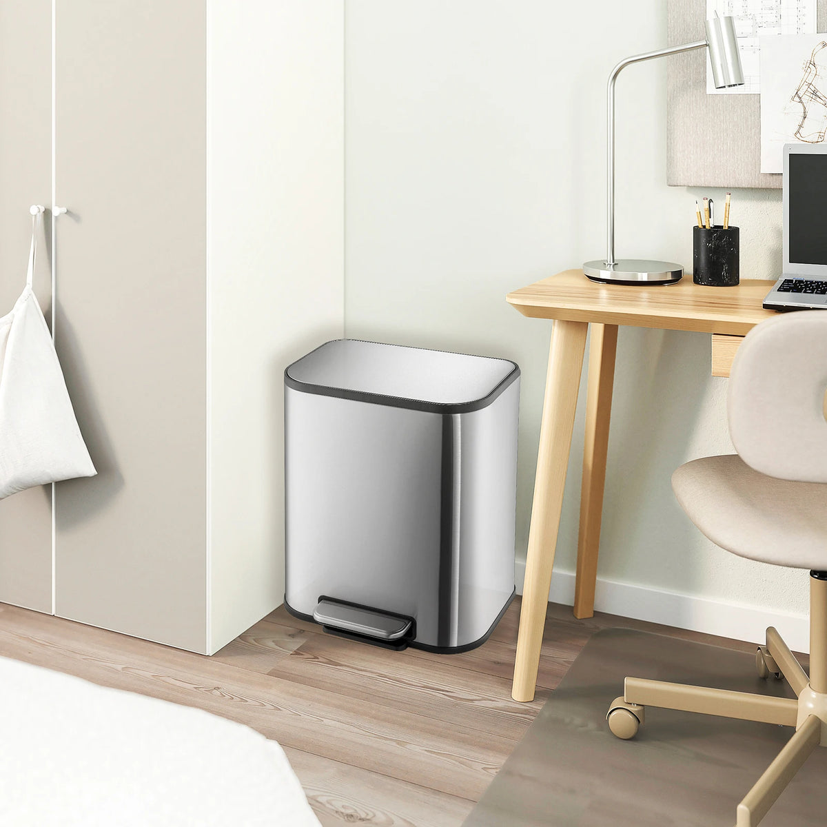 A modern stainless steel trash can with a soft-close lid and step pedal sitting on a wooden desk.